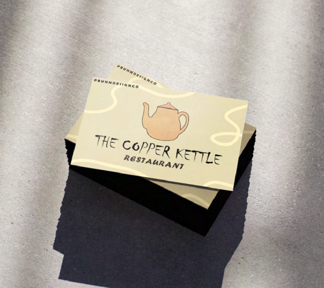 A cream Copper Kettle business card with the teapot logo, photographed on textured fabric.