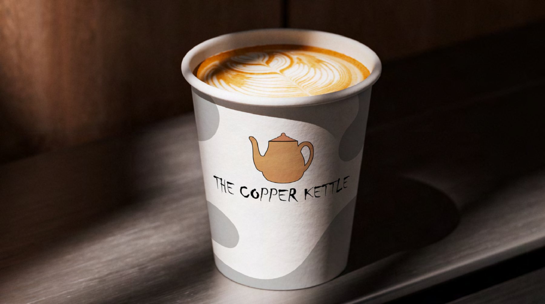 A paper takeaway cup printed with The Copper Kettle teapot logo, resting on a dark wooden ledge.
