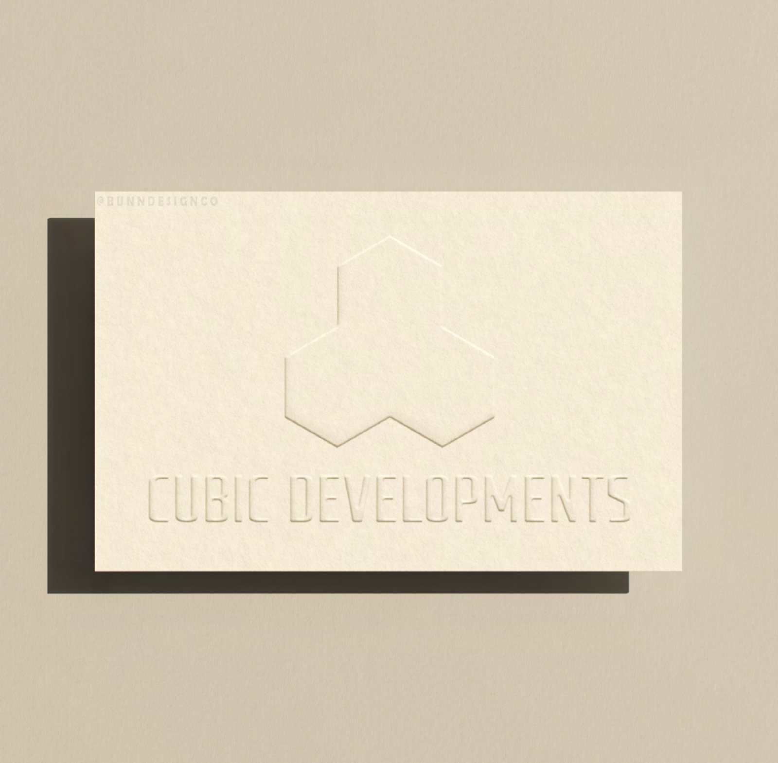 A Cubic Developments business card with a blind-embossed cube logo on textured stone-coloured stock.