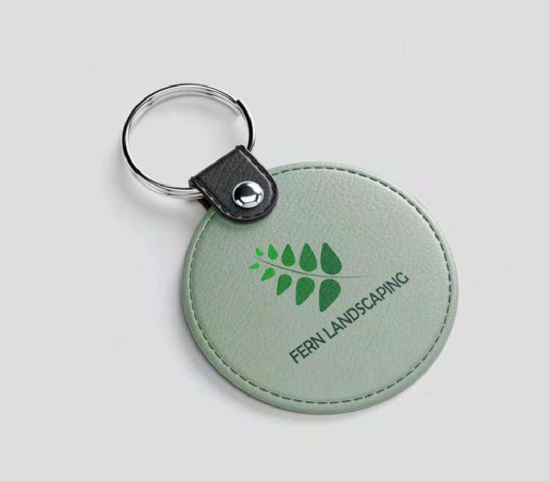 A round green leather keychain stamped with the Fern Landscaping frond logo.