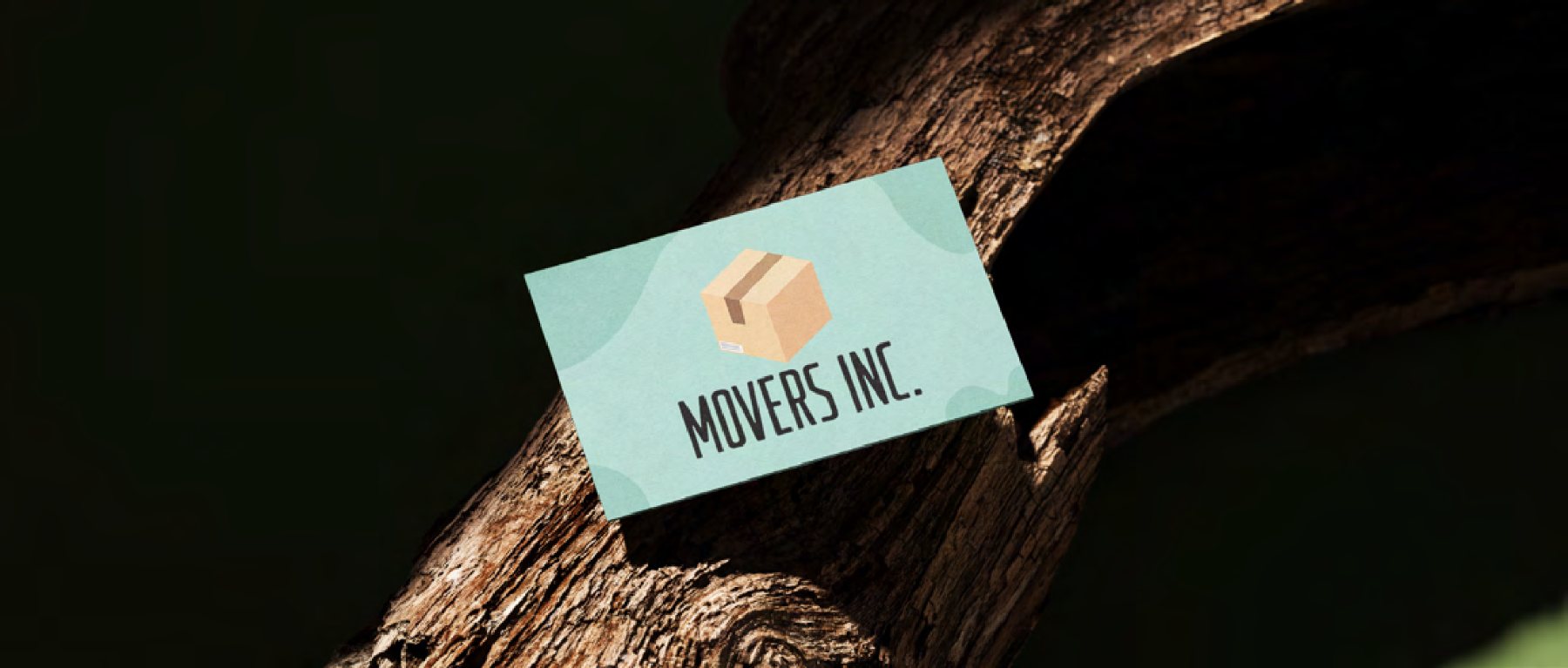 A teal Movers Inc. business card with a parcel-box logo, balanced against tree bark.