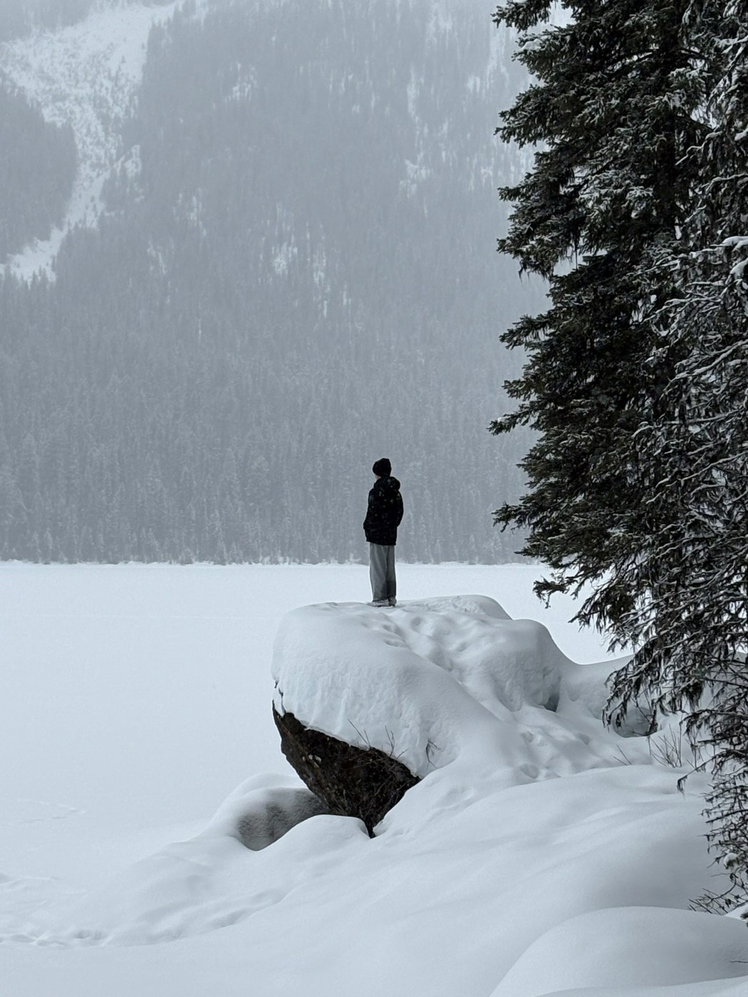 Noah Bunn standing on a snow-covered rock overlooking a frozen lake and mountains