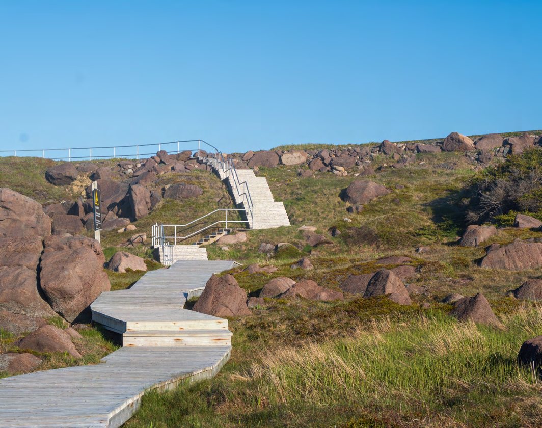 A wooden boardwalk and staircase winding between large pink granite boulders and scrub grass.