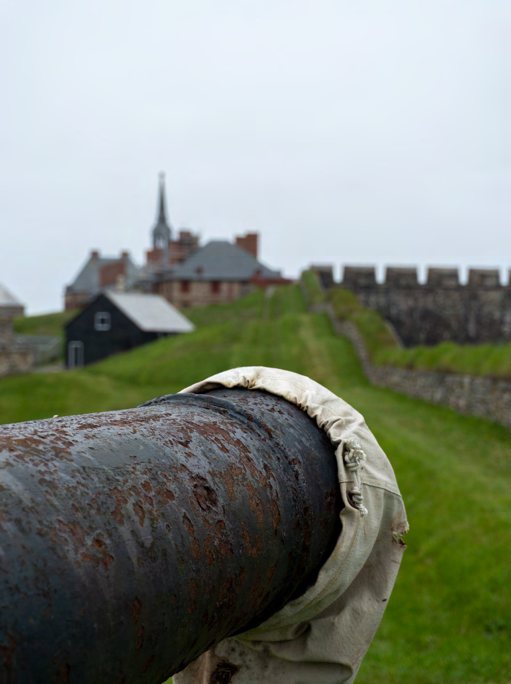 A weathered iron cannon barrel in the foreground with a fortified building behind it.