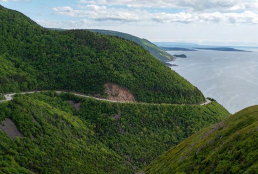 A road curving along a steep green hillside above the sea.