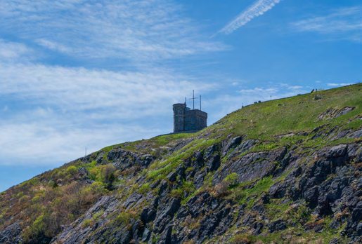 A grassy hillside rising to a stone tower silhouetted against a bright sky.